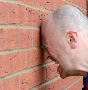 A man banging his head against the wall in frustration.