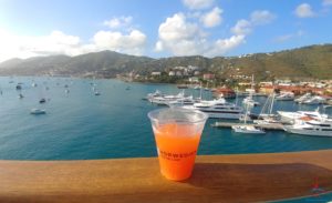 a cup of orange juice on a railing overlooking a body of water