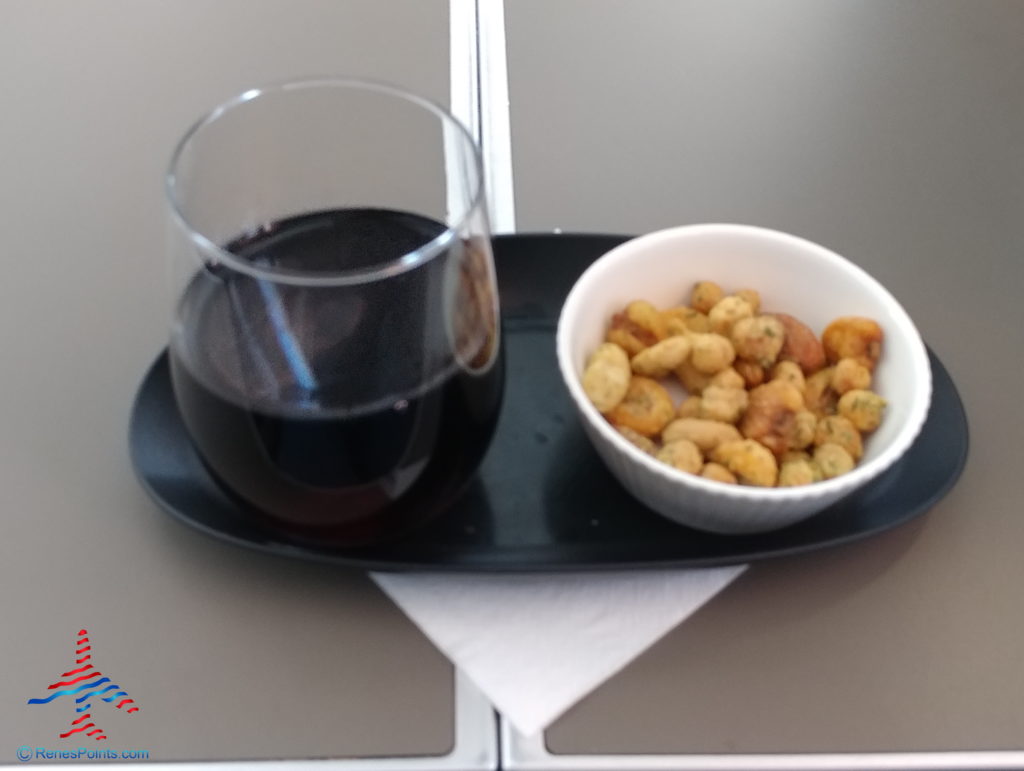 a glass of wine and a bowl of peanuts on a tray