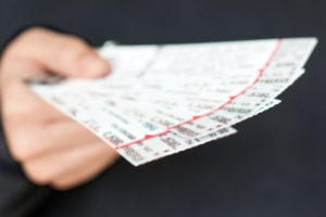 Tickets to a show / event in a hand with a black background. Photo credit: @iStock.com/GlasserStudios