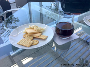 Cheese, crackers, and Camelot red wine are seen atop a glass table on the deck of the United Club LAX airport lounge in Los Angeles, California. © Chris Carley / PointsLounge.