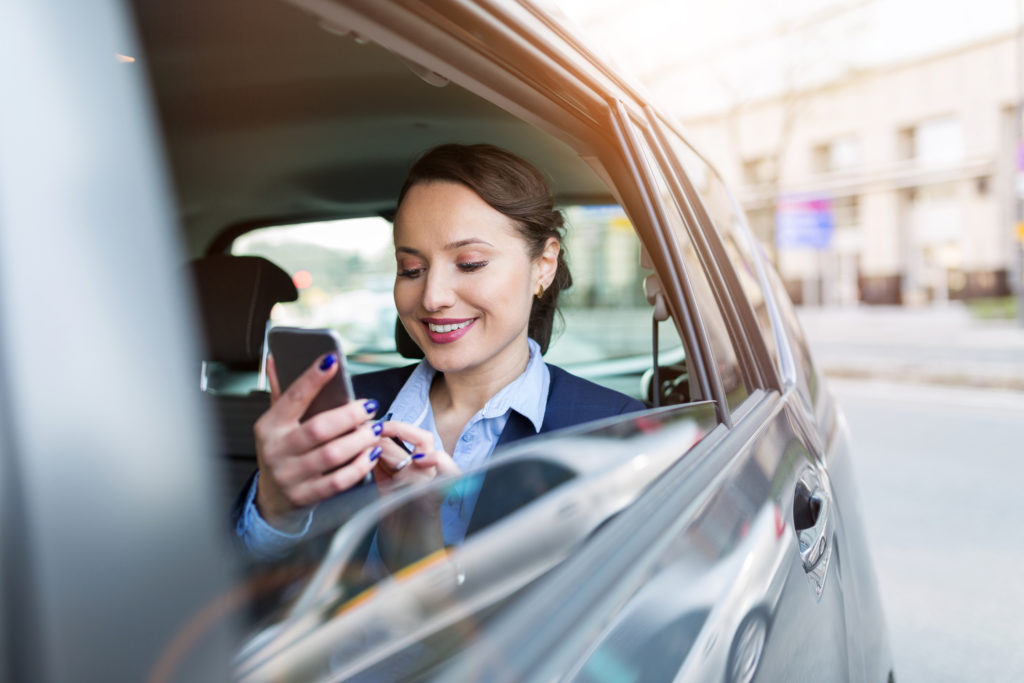 Young businesswoman on the back seat with smart phone