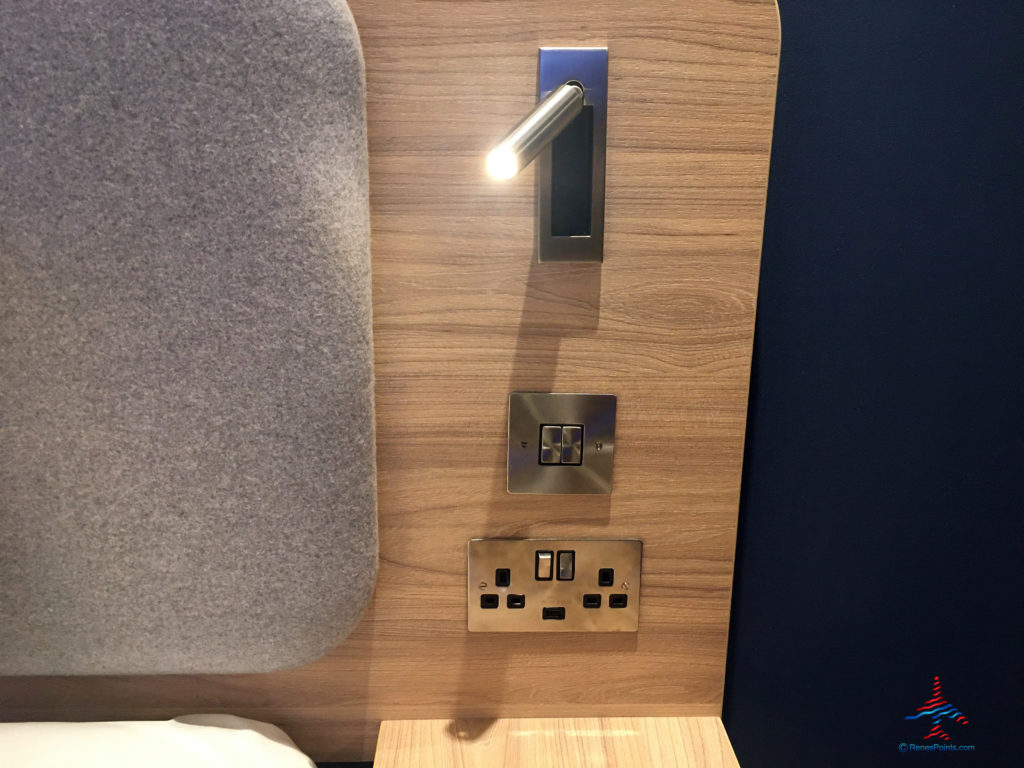 A nightstand, power outlets, and reading lamp are seen inside a room at the Holiday Inn Express London Heathrow T4 (LHR airport hotel) in Hounslow, United Kingdom.