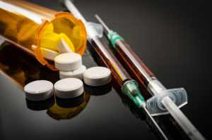 Opioid epidemic, drug abuse concept with closeup on two heroin syringes or other narcotics surrounded by scattered prescription opioids. Oxycodone is the generic name for a range of opioid painkillers (Photo credit: ©iStock.com/Moussa81)