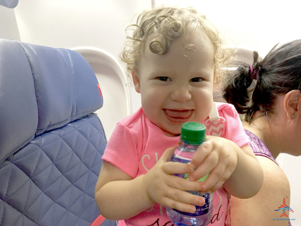 A female toddler smiles while opening a bottle of water at a first class seat on a Delta Air Lines flight.