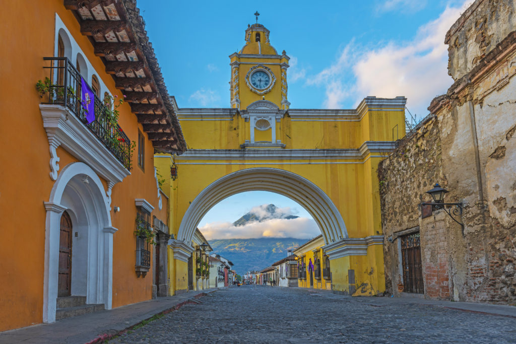 The Agua volcano illuminated by the first sunlight at sunrise seen from the main street of Antigua city, famous for its yellow arch, Guatemala, Central America.