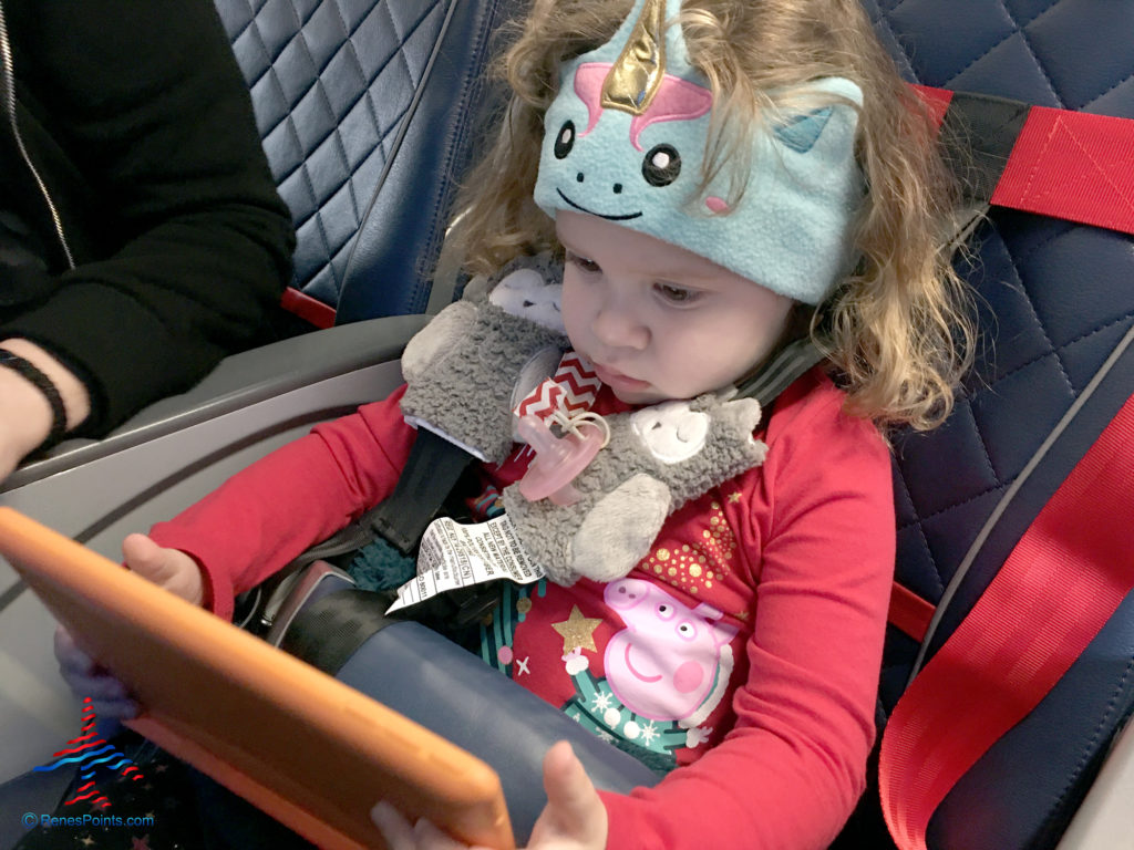 A toddler -- wearing an airplane harness and unicorn headphone with built-in earphones -- watches a tablet during a Delta Air Lines flight.