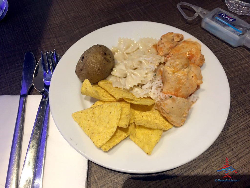A meal plate with potatoes, pasta, chicken cacciatore, and corn chips is seen at the Plaza Premium Arrivals Lounge at London Heathrow Airport Terminal 4.
