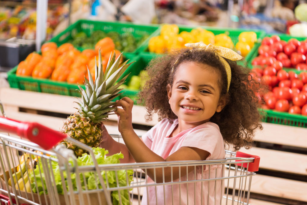 Smiling child holding a pineapple while grocery shopping in a supermarket