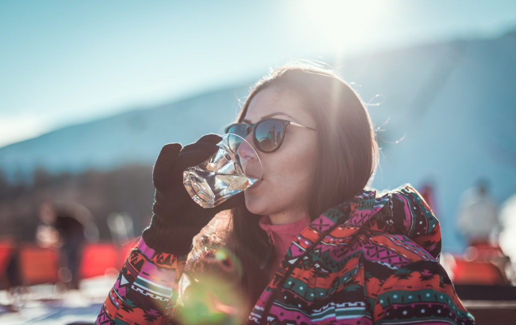 Close-up of a young single woman in a ski-wear drinking cocktail while sitting on a chair at the coffee place in the ski resort