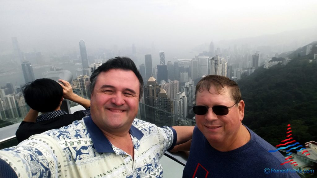 two men standing on a balcony with a city in the background