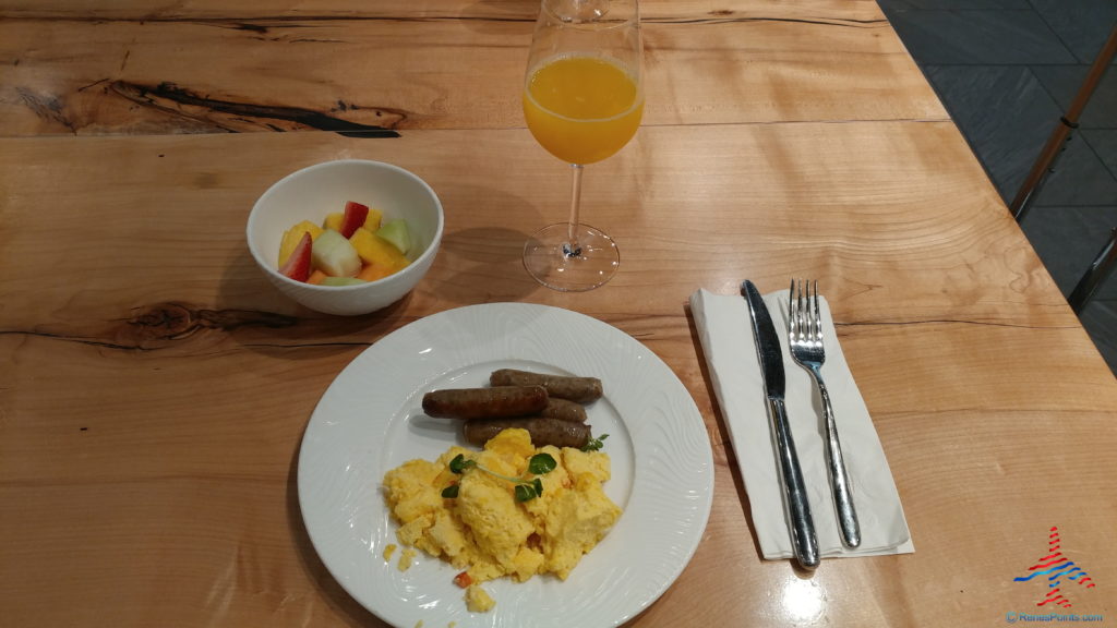 a plate of scrambled eggs and sausages with fruit and a glass of juice