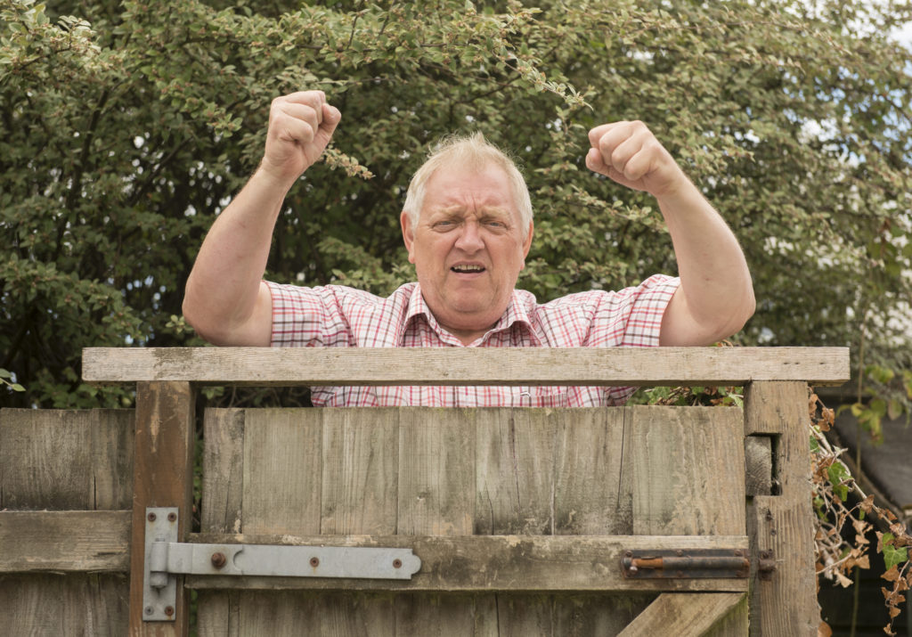 An angry neighbor shouting and shaking his fists over a fence in the garden